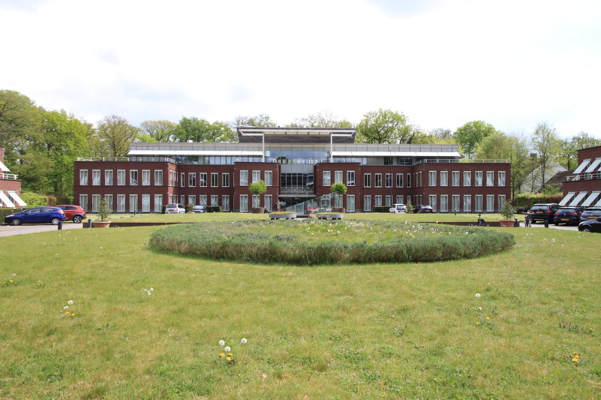 Modern kantoorgebouw aan de Arnhemse Bovenweg met een verzorgd gazon en geparkeerde auto's op de voorgrond.